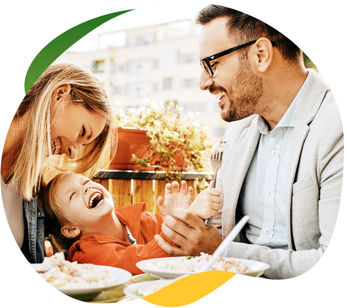 Tööriietes noored vanemad söövad söögilaua ääres, nende vahel istub laps. Nad naeravad ja neil on koos tore.