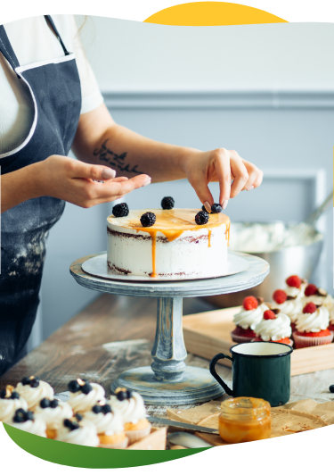 Köögis seisev inimene kaunistab kooki marjadega. Tööpinnal on mitu muffinit.