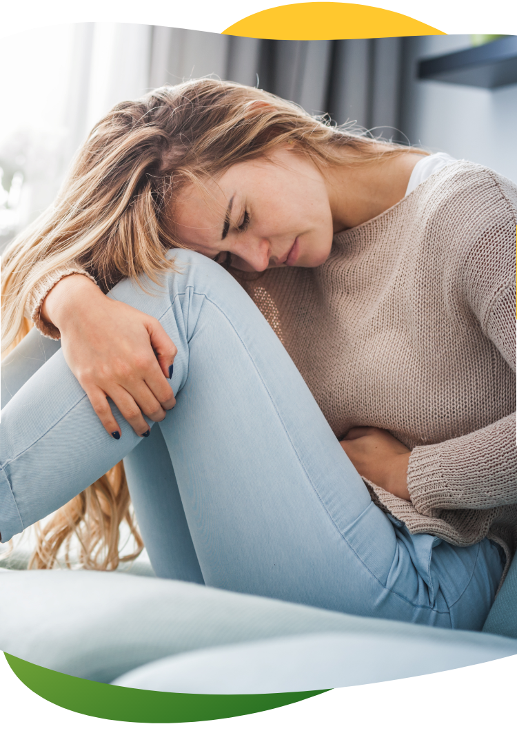 Noor naine kannatab menstruatsiooniga seotud kõhupuhituse käes ja istub kägaras põrandal, hoides vasaku käega kõhust.